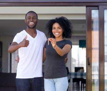 Afrikanisches Paar, das auf Terrasse steht, hält Schlüssel des neuen Hauses