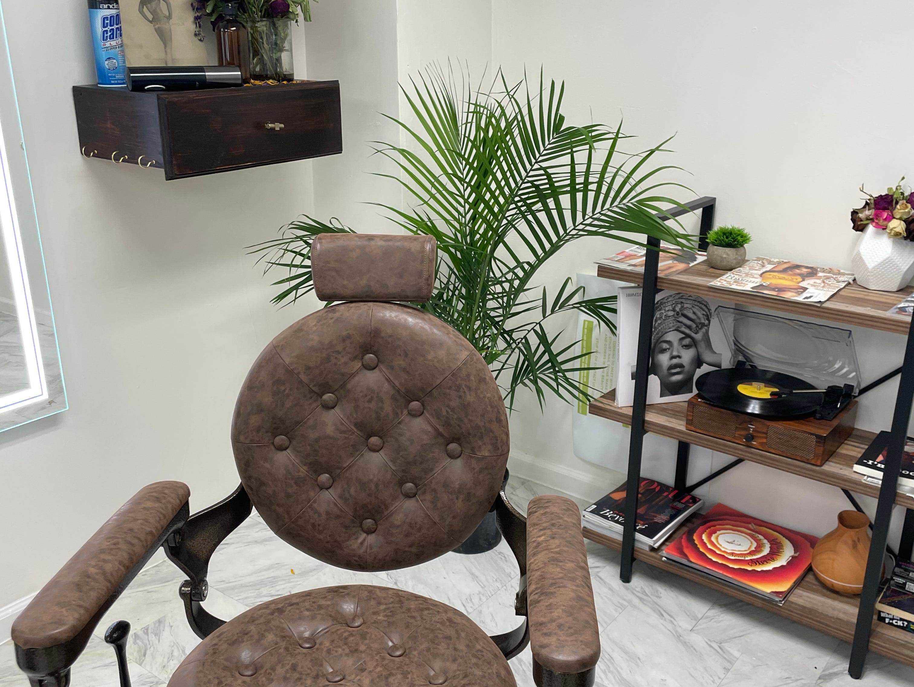 Ein brauner Friseurstuhl aus Leder steht vor einem kleinen Regal mit Schallplatten in Enkel's Barbershop.