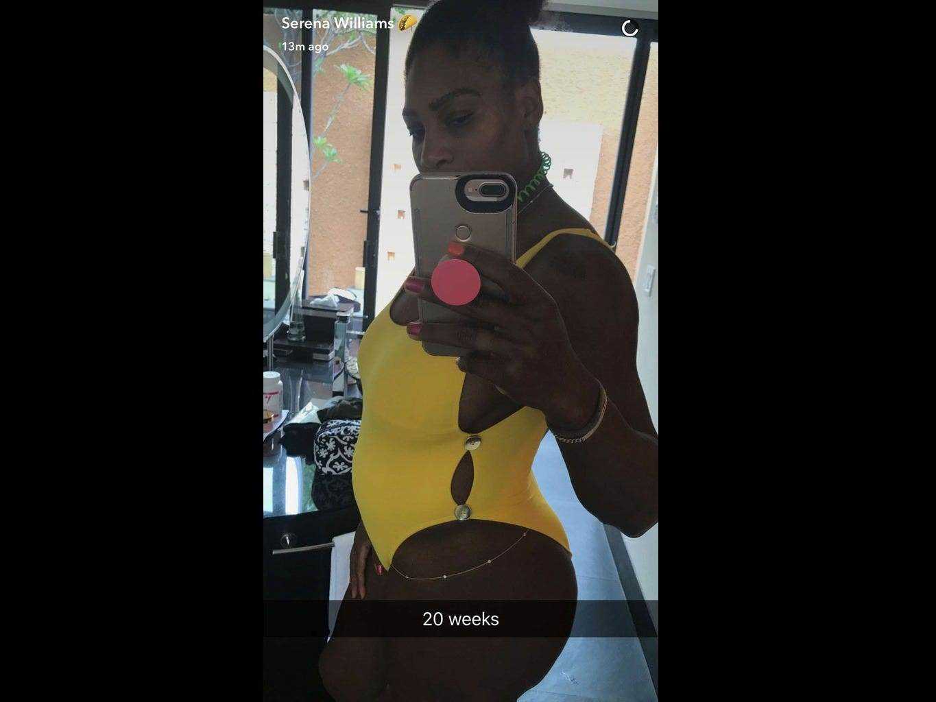 Serena Williams in einem gelben Badeanzug zeigt ihren Babybauch im Spiegel.