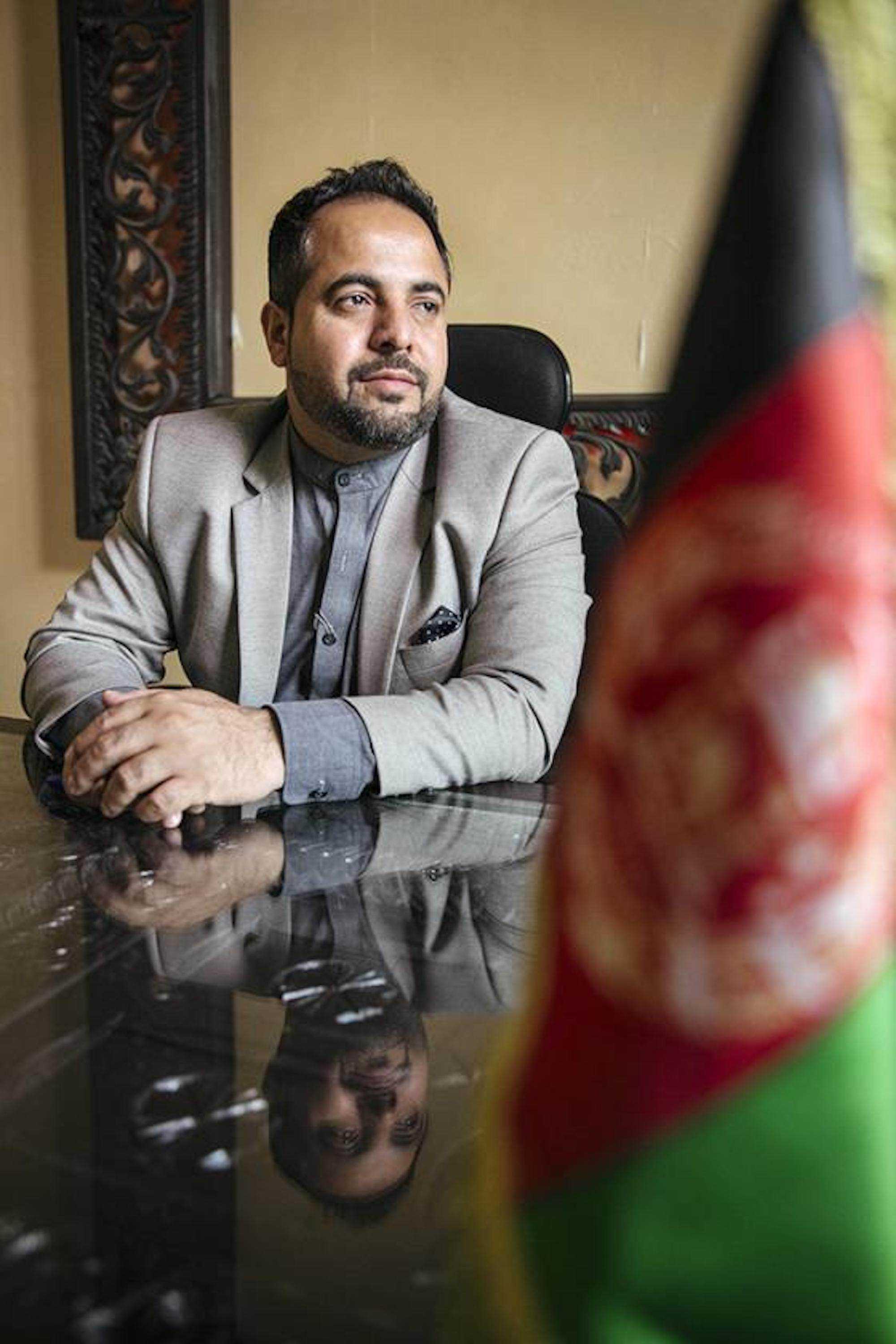Hamid Samar sitzt an einem Tisch, im Vordergrund die Flagge Afghanistans.