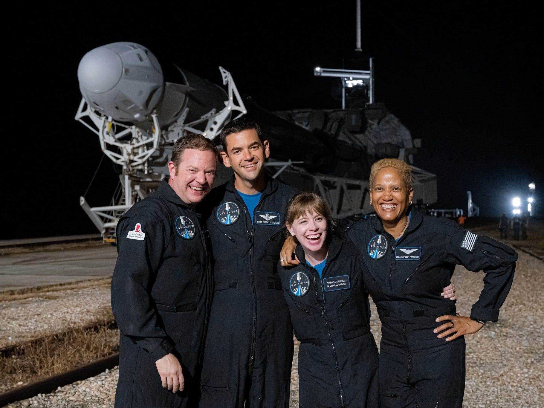 Die Crew von inspiration4 posiert vor der Falcon 9-Rakete, die nachts seitlich auf der Landebahn liegt