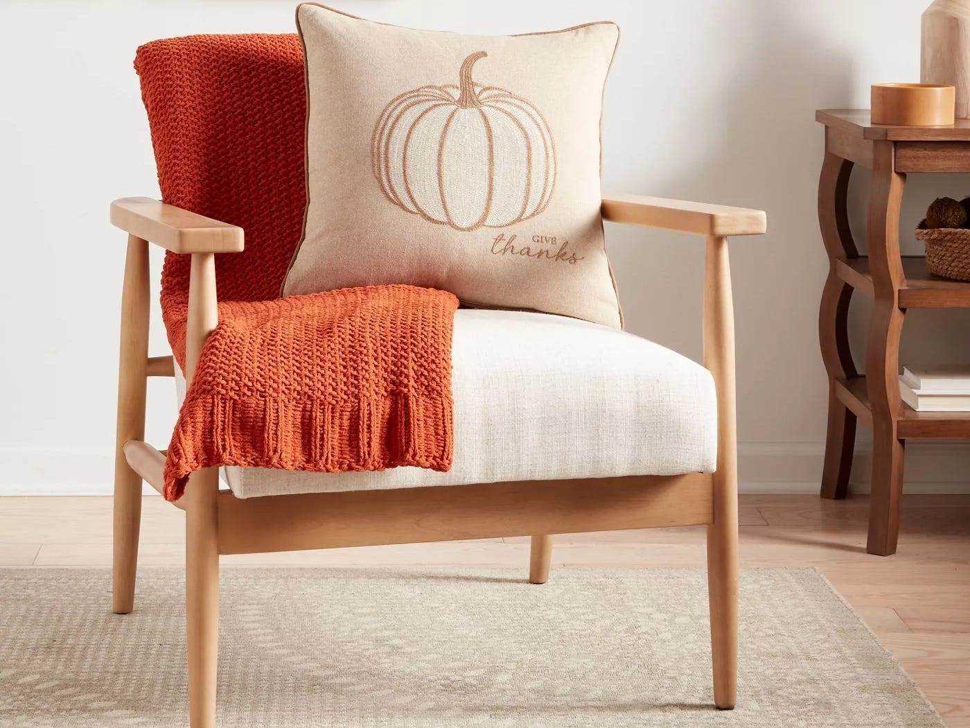 Bild eines Stuhls mit einem Kürbis-Wurfkissen und einer orangefarbenen Decke darauf von Target, dem süßesten Herbstdekor bei Target 2021