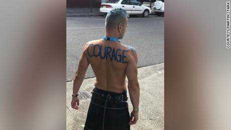 Stark mit dem Wort "Mut"  auf seinem Rücken, bevor er im März 2019 beim Sydney Gay and Lesbian Mardi Gras marschierte. Jetzt hat er das Wort auf seinem Rücken tätowiert.