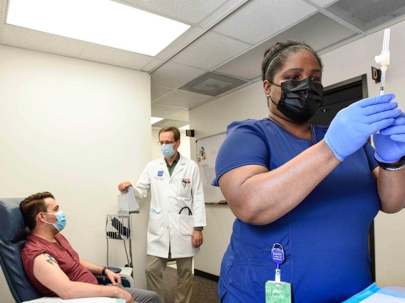 Frau in Peelings bereitet Covid-19-Impfstoff vor, während Patient und Arzt im Hintergrund chatten