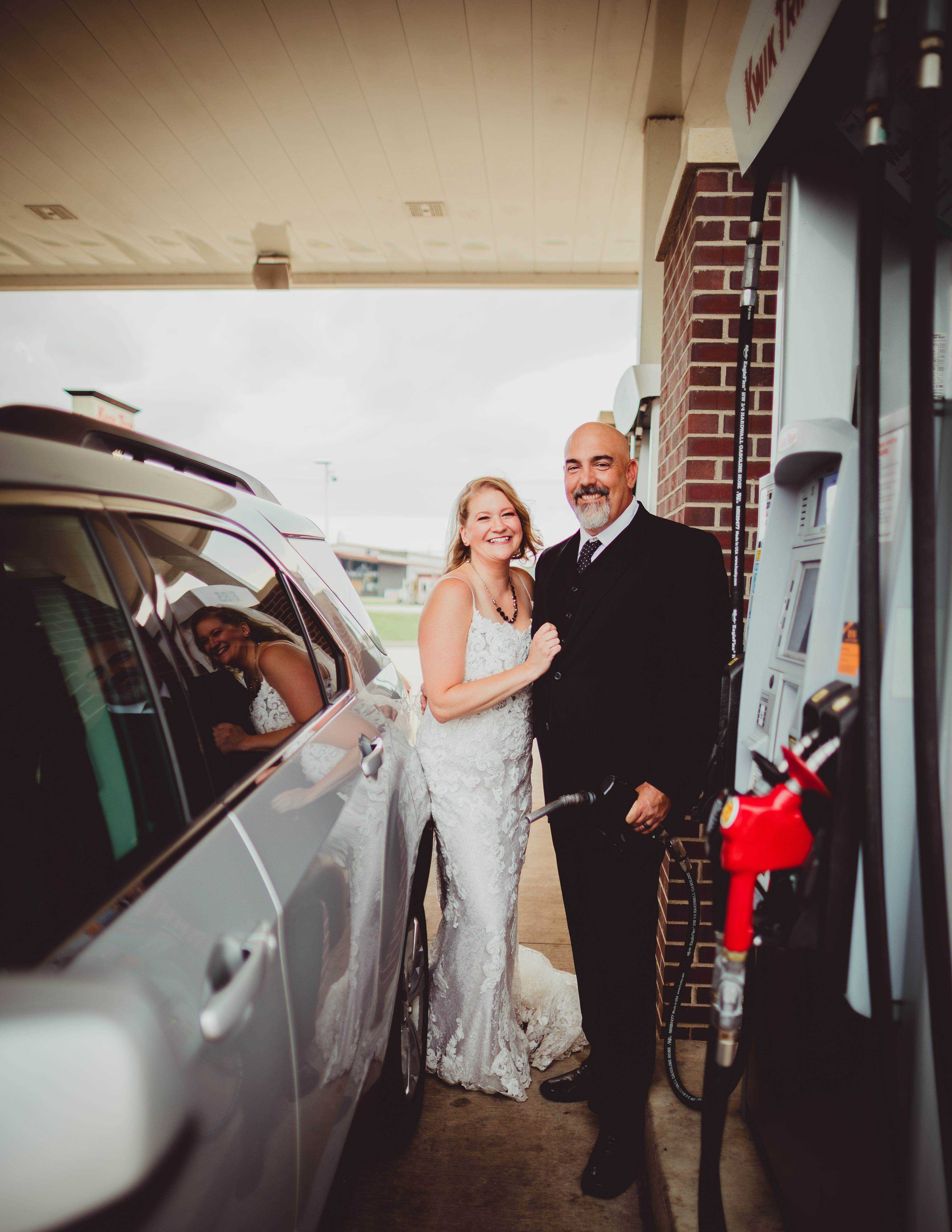 Ein Brautpaar posiert an der Zapfsäule einer Tankstelle