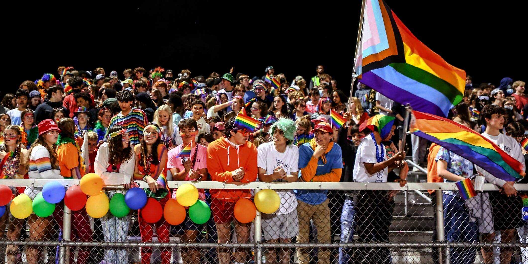 Die Menge beim Heimkehrspiel der Burlington High School jubelt den Künstlern zu, während sie in Regenbogenfarben geschmückt sind.