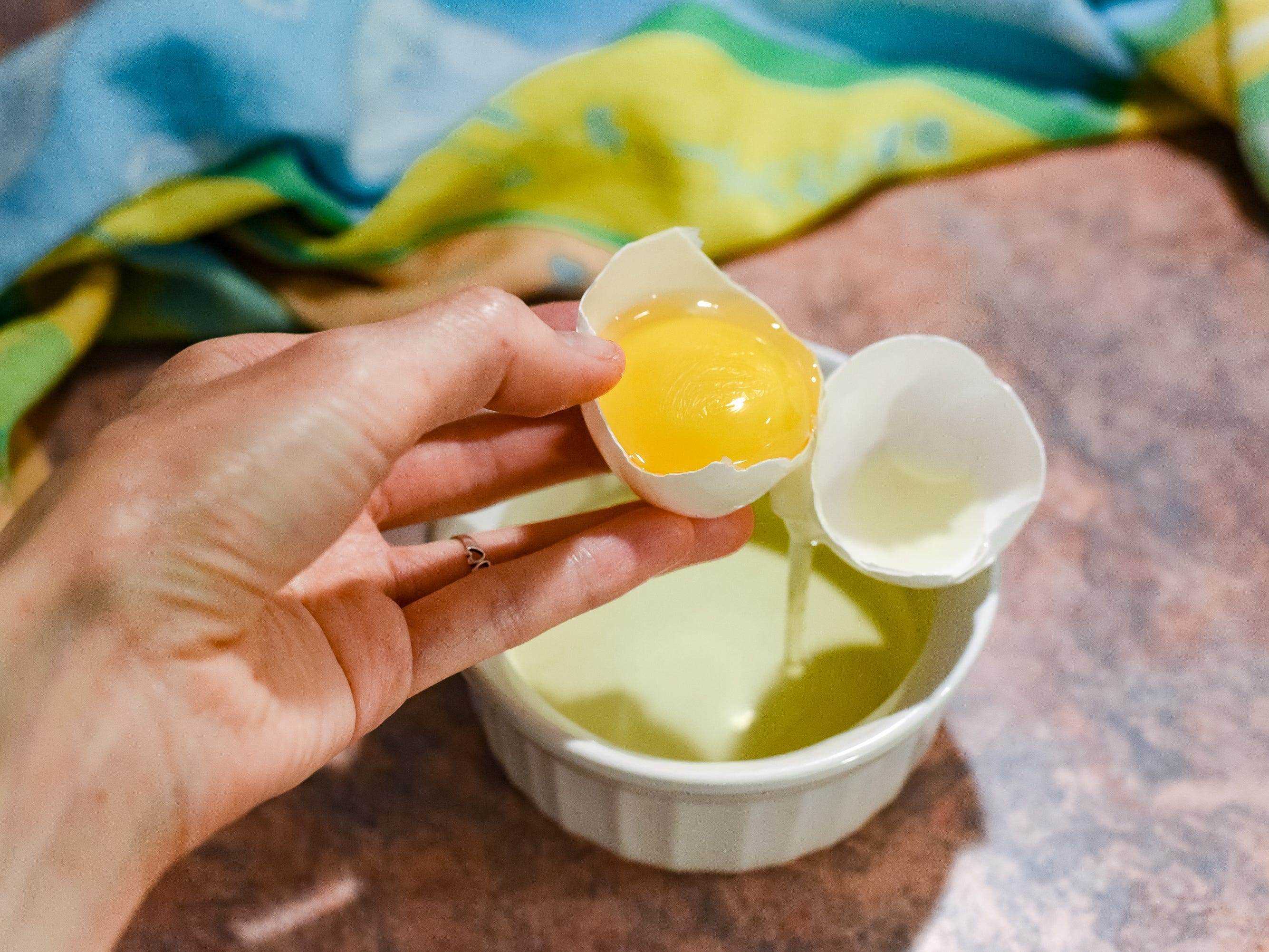 Eine Hand knackt ein Ei in einem Auflaufförmchen.