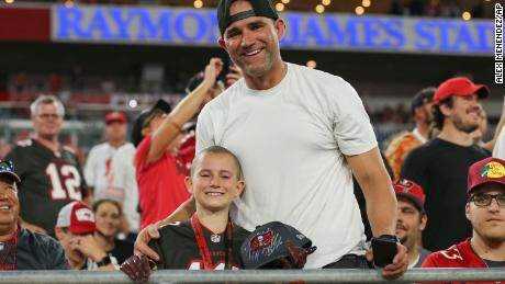 Der Krebsüberlebende Noah Reeb und sein Vater lächeln, nachdem Brady ihm einen Hut überreicht hat.