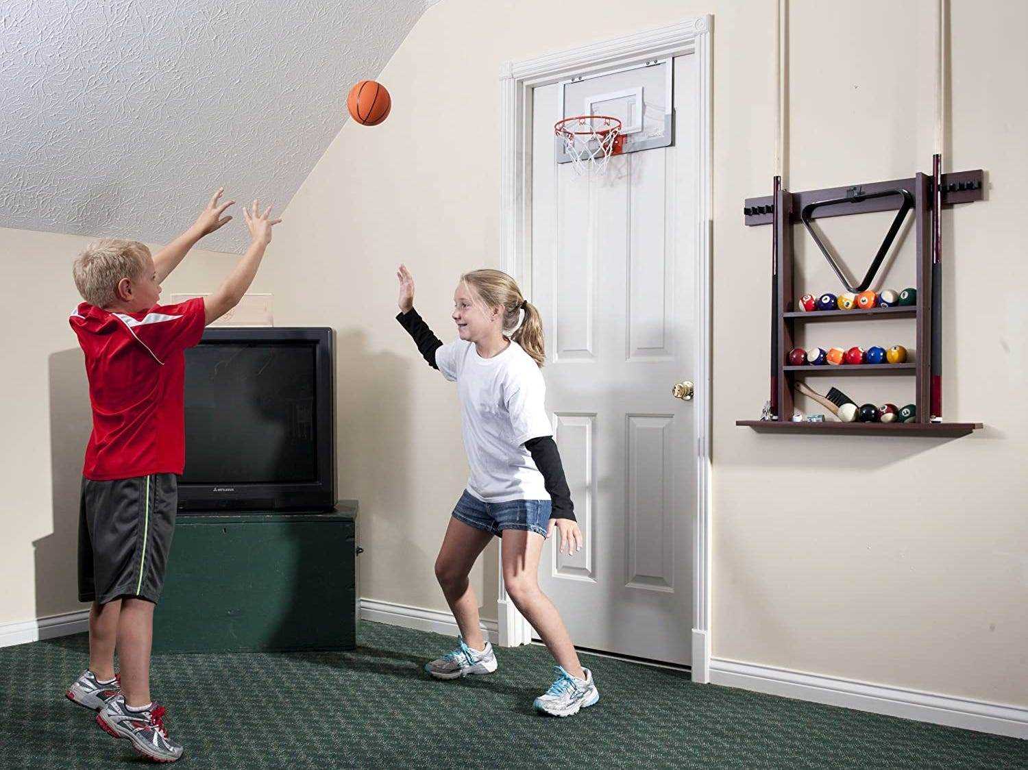 Ein Junge schießt mit einem Spielzeugbasketball auf einen Basketballkorb über der Tür, während ein Mädchen ihn blockiert