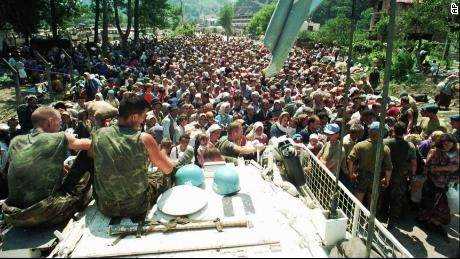 Niederländische UN-Friedenstruppen sitzen auf einem Fahrzeug, während sich am 13. Juli 1995 muslimische Flüchtlinge aus Srebrenica im nahegelegenen Dorf Potocari versammeln. 