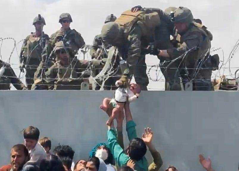 Ein Baby wird von einem US-Soldaten gepackt und über einen Stacheldrahtzaun gehoben.