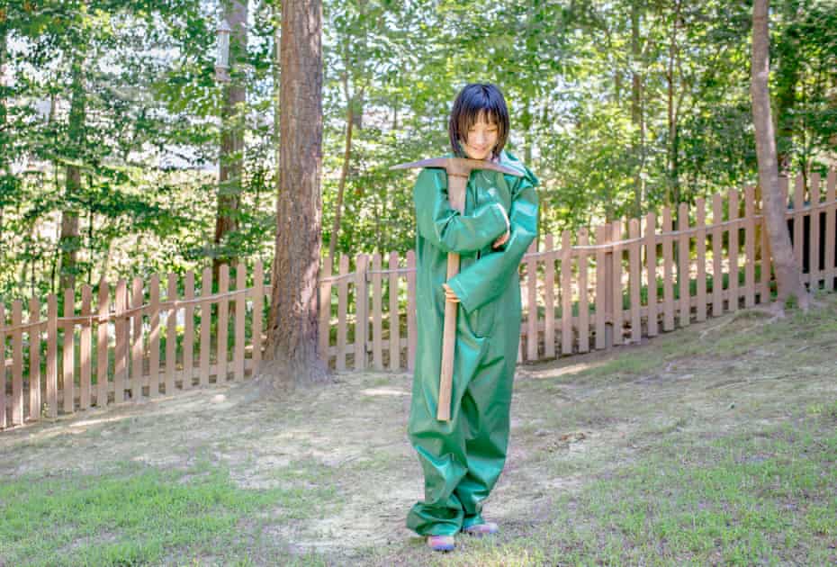 Mia, ein Mädchen mit Autismus-Spektrum, fotografiert in einem grünen Gummianzug, eine Spitzhacke haltend, mit Bäumen im Rücken, 2016