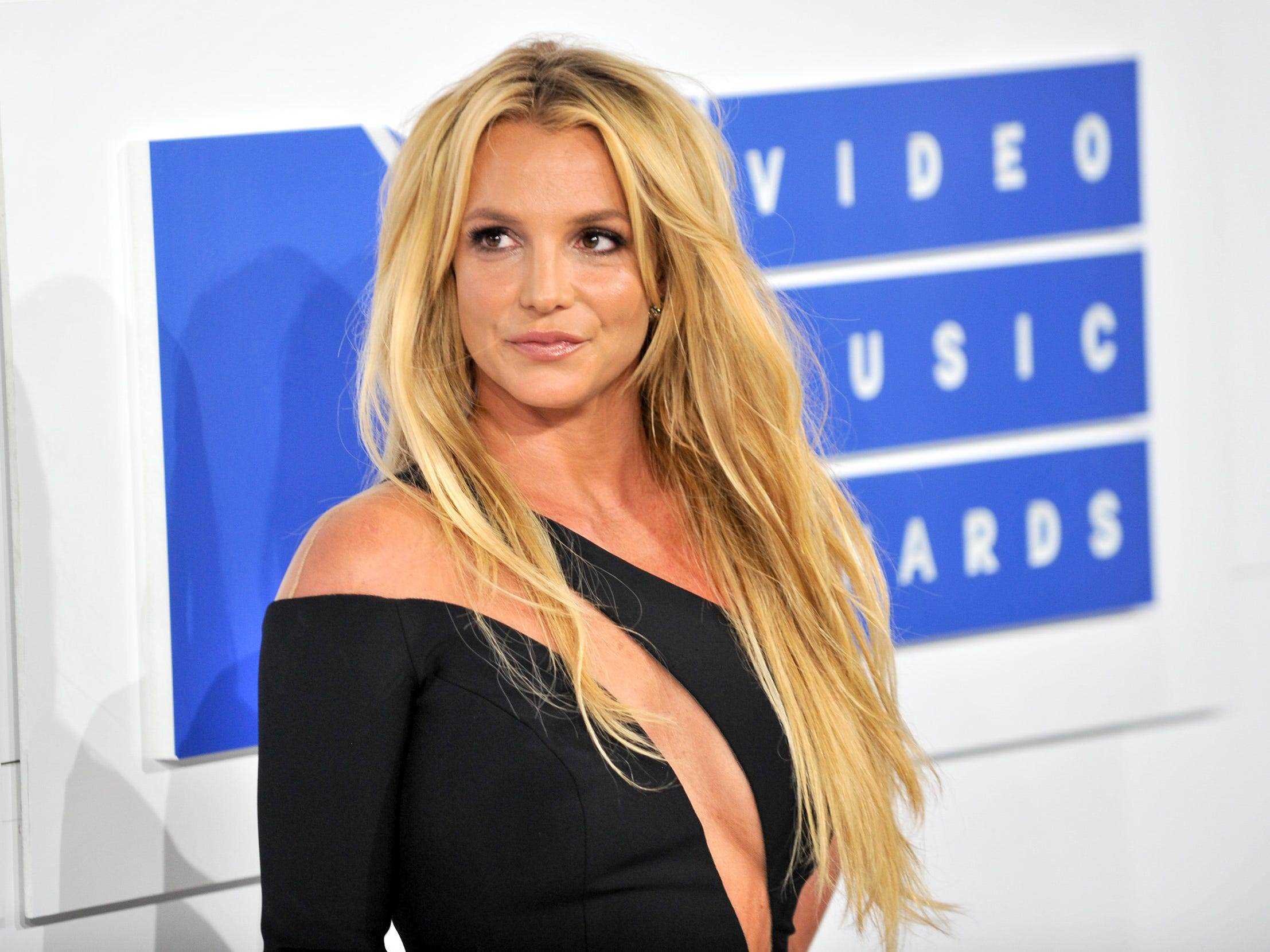 Britney Spears, mit ihren blonden Haaren nach unten gestylt und trug ein schwarzes langärmeliges Kleid, auf dem roten Teppich der MTV VMAs im Jahr 2016.