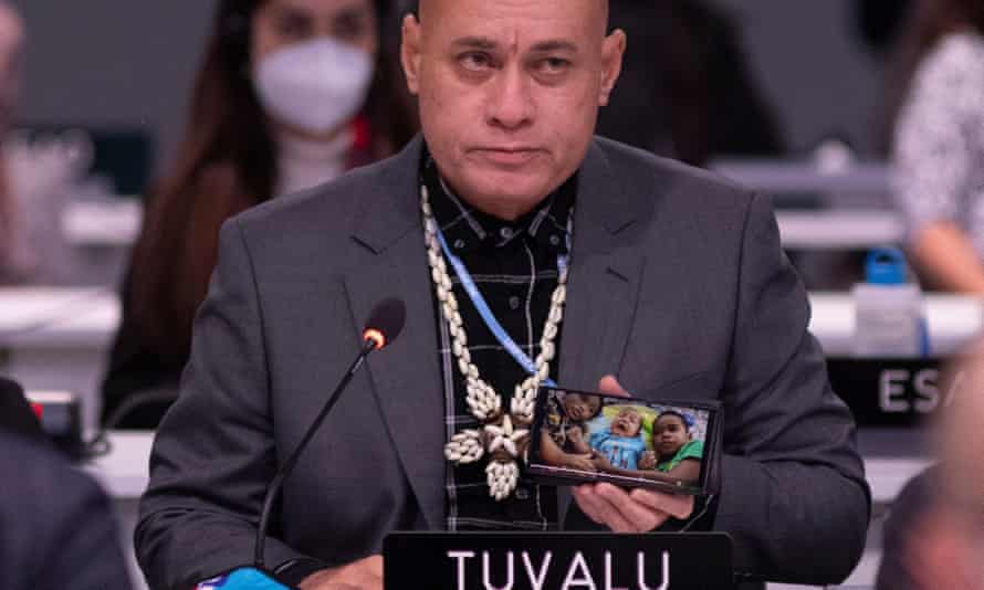 Ein Delegierter aus Tuvalu hält auf seinem Handy ein Foto von drei Kindern hoch und spricht während einer Plenarsitzung bei Cop26.
