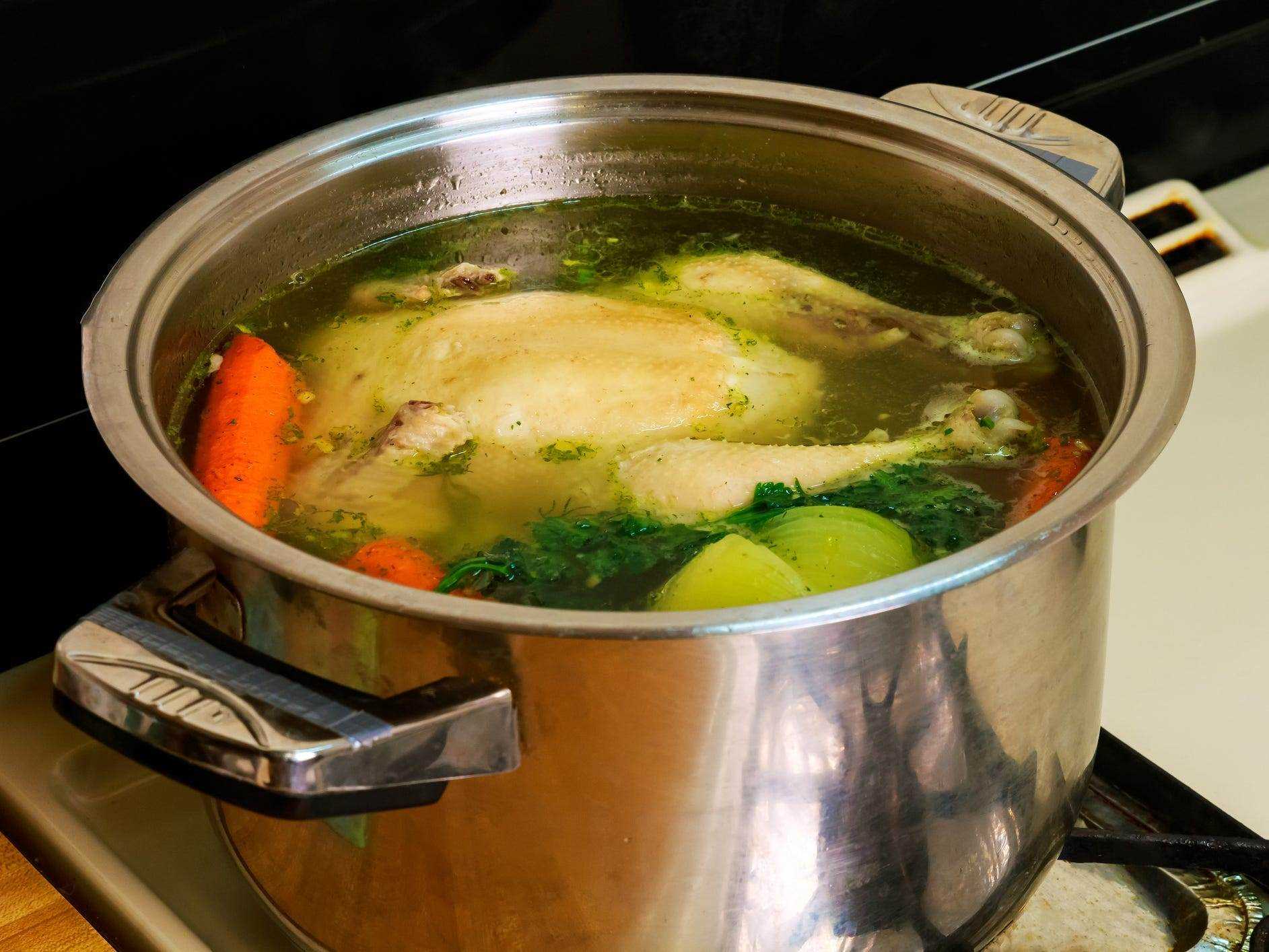 Ein ganzes Huhn, das in einem Topf mit Wasser mit Kräutern und Gemüse gekocht wird