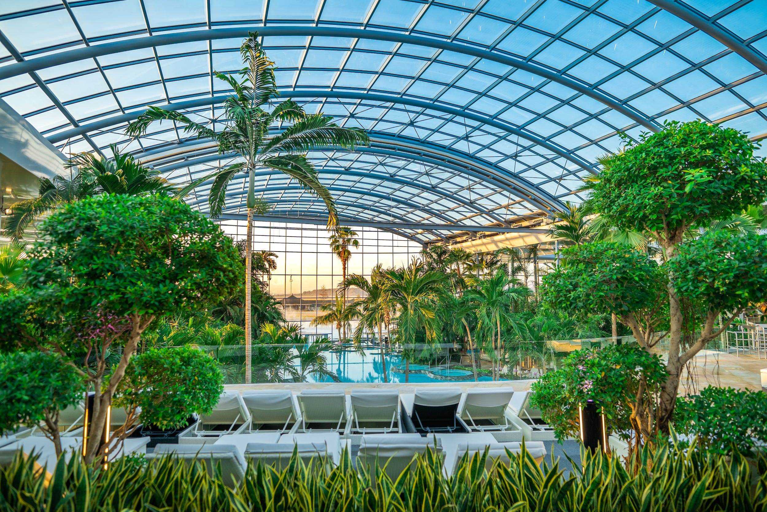 Lounge-Sitzplätze an einem Pool neben Pflanzen unter einer transparenten Kuppel