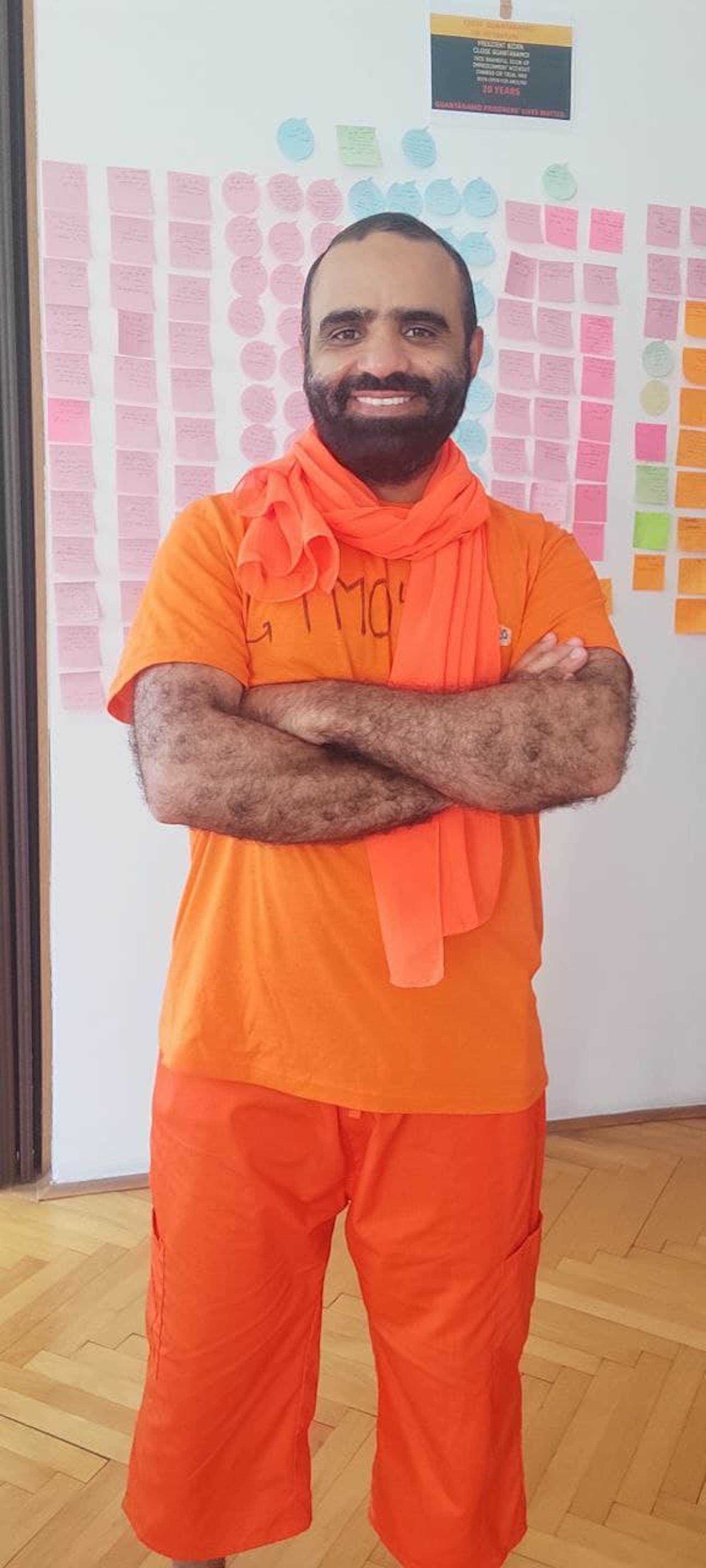 Mansoor Adayfi, orange gekleidet, steht vor einer Wand aus Post-its.