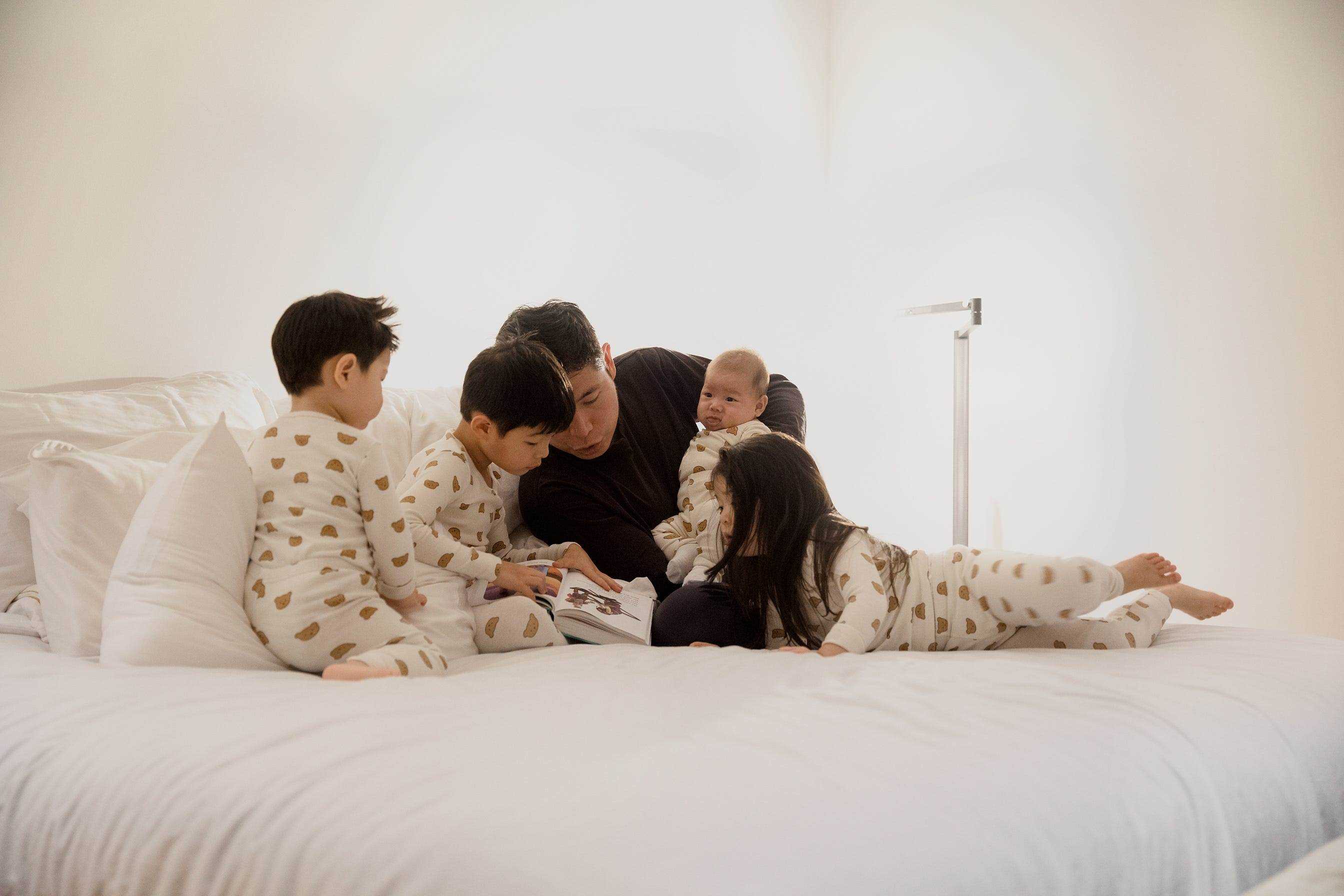 Anthony Tan auf einem Bett mit seinen Kindern, die eine Gutenachtgeschichte lesen.