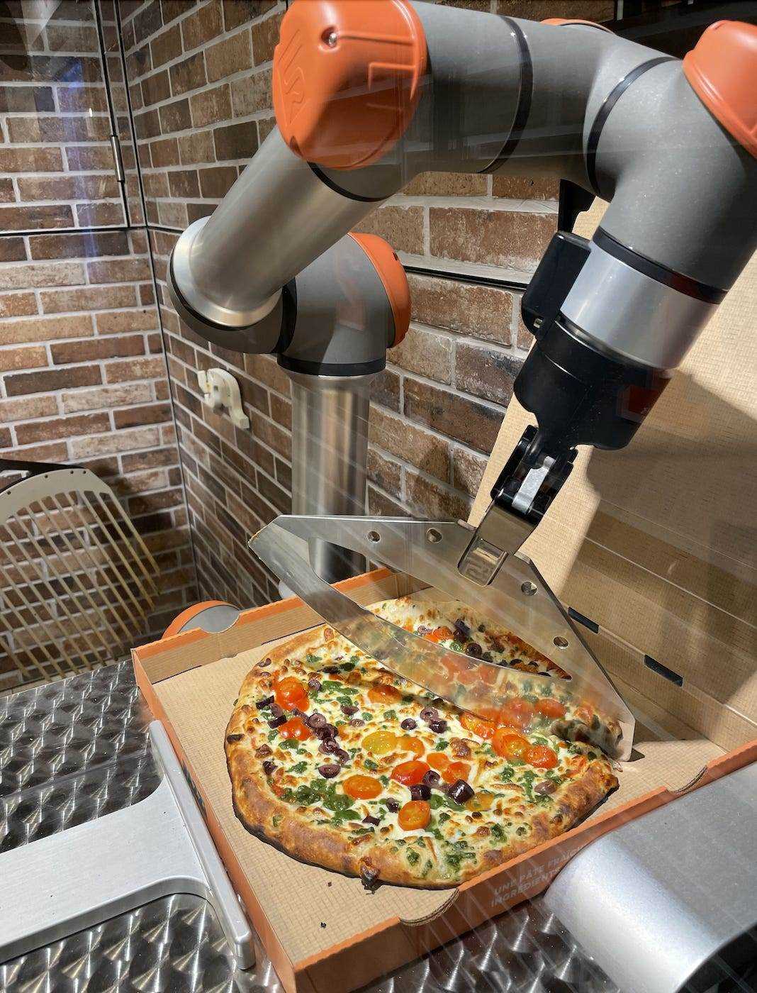 Ein Roboterarm schneidet eine Pizza in einem Karton