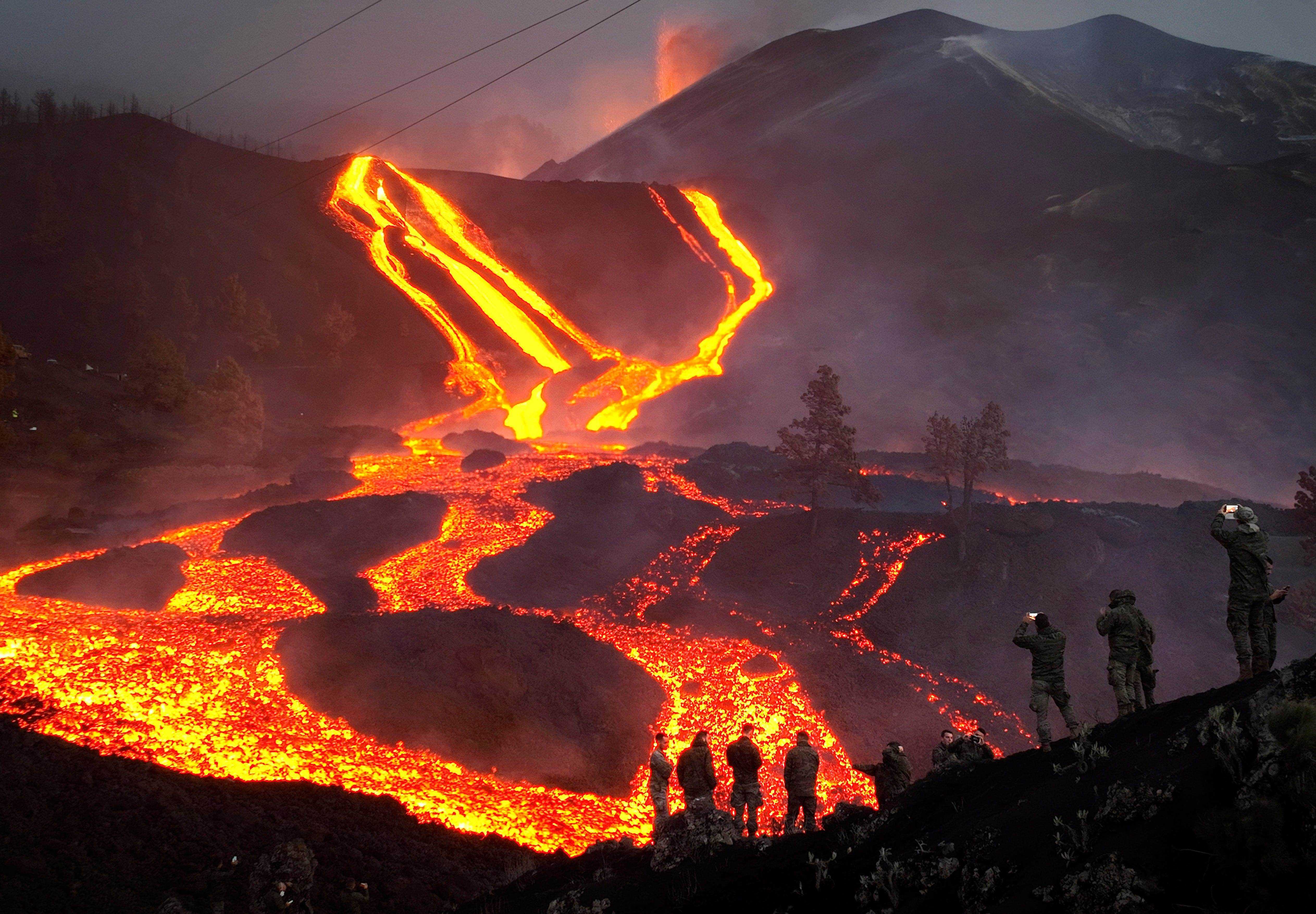 Spanische Armeesoldaten stehen auf einem Hügel, während Lava beim Ausbruch eines Vulkans fließt.