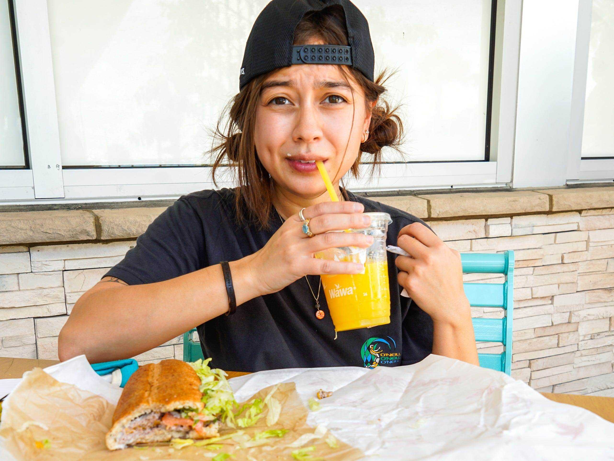 Die Autorin schlürft ihren Orangensaft außerhalb von Wawa mit ihrem Sandwich auf dem Tisch vor ihr