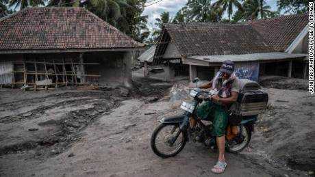 Ein Mann fährt am 6. Dezember 2021 mit einem Fahrrad an beschädigten Häusern im Dorf Sumber Wuluh in Lumajang vorbei.