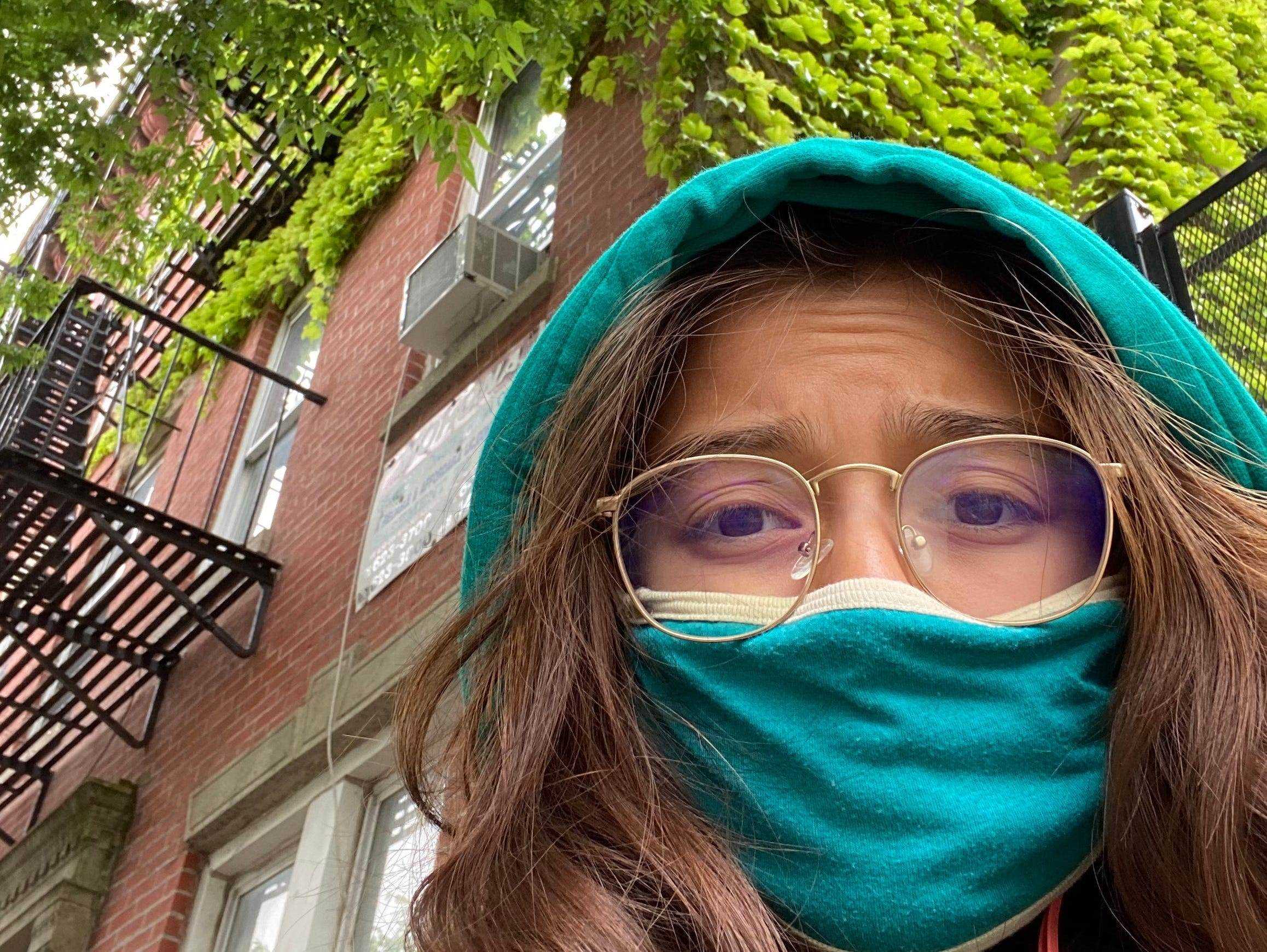 Die Autorin ist vor ihrer Wohnung in Brooklyn zu sehen und trägt einen türkisfarbenen Hoodie und eine Maske