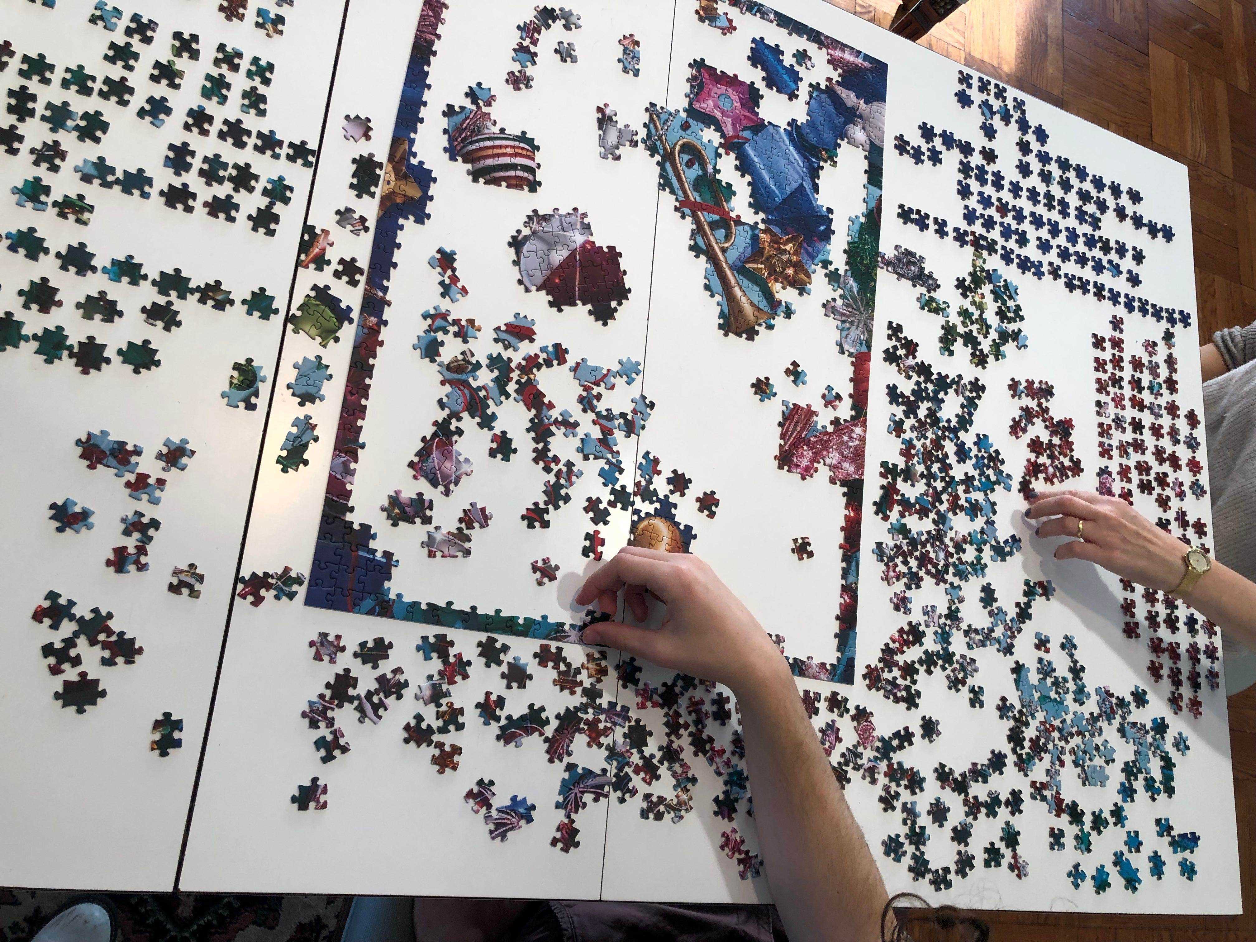 1.000 Puzzles verteilt auf einem großen Tisch mit Händen, die Teile bewegen