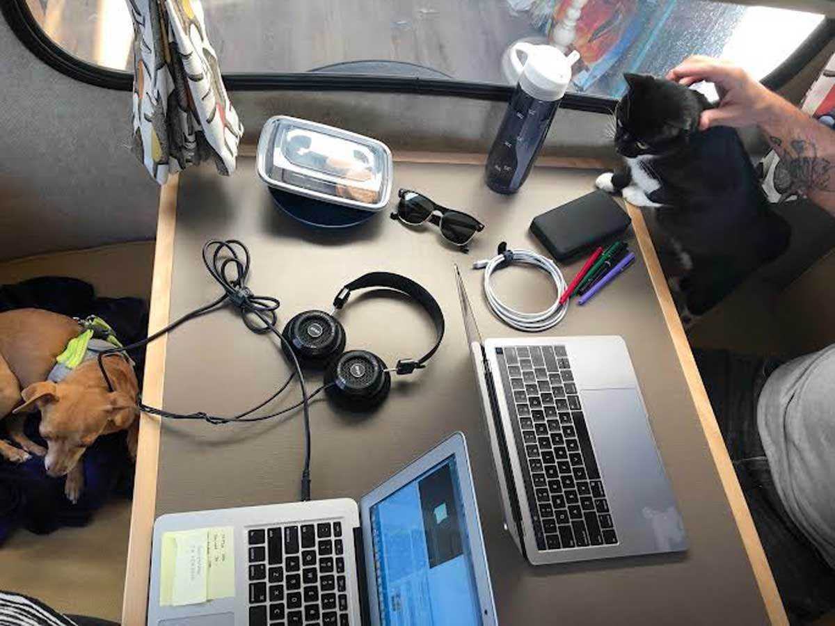 Ein Tisch in einem Wohnwagen mit Computern, Haustieren und Mahlzeiten.