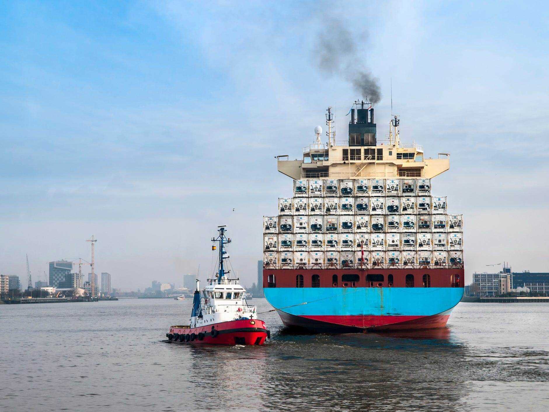 Rückansicht eines großen Frachtschiffs, das von einem Schlepper im Hafen von Rotterdam, Niederlande, manövriert wird.