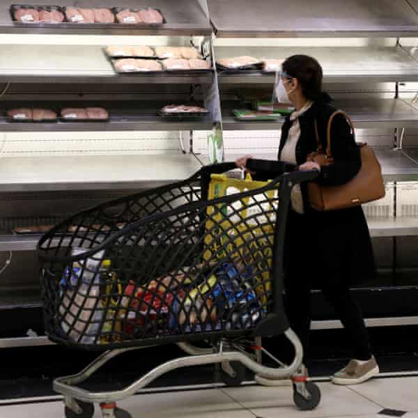 Eine Frau schiebt einen Einkaufswagen in einem Supermarkt an fast leeren Regalen vorbei