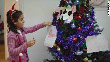 Eines der Kinder von INARA platziert eine Dekoration, die sie mit ihren darauf geschriebenen Weihnachtswünschen angefertigt hat, auf einen Weihnachtsbaum.