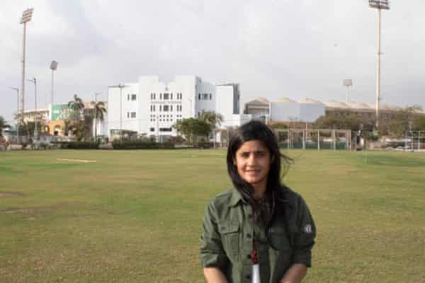 Eine Frau steht auf einem Cricketfeld mit einem großen weißen Pavillon im Hintergrund
