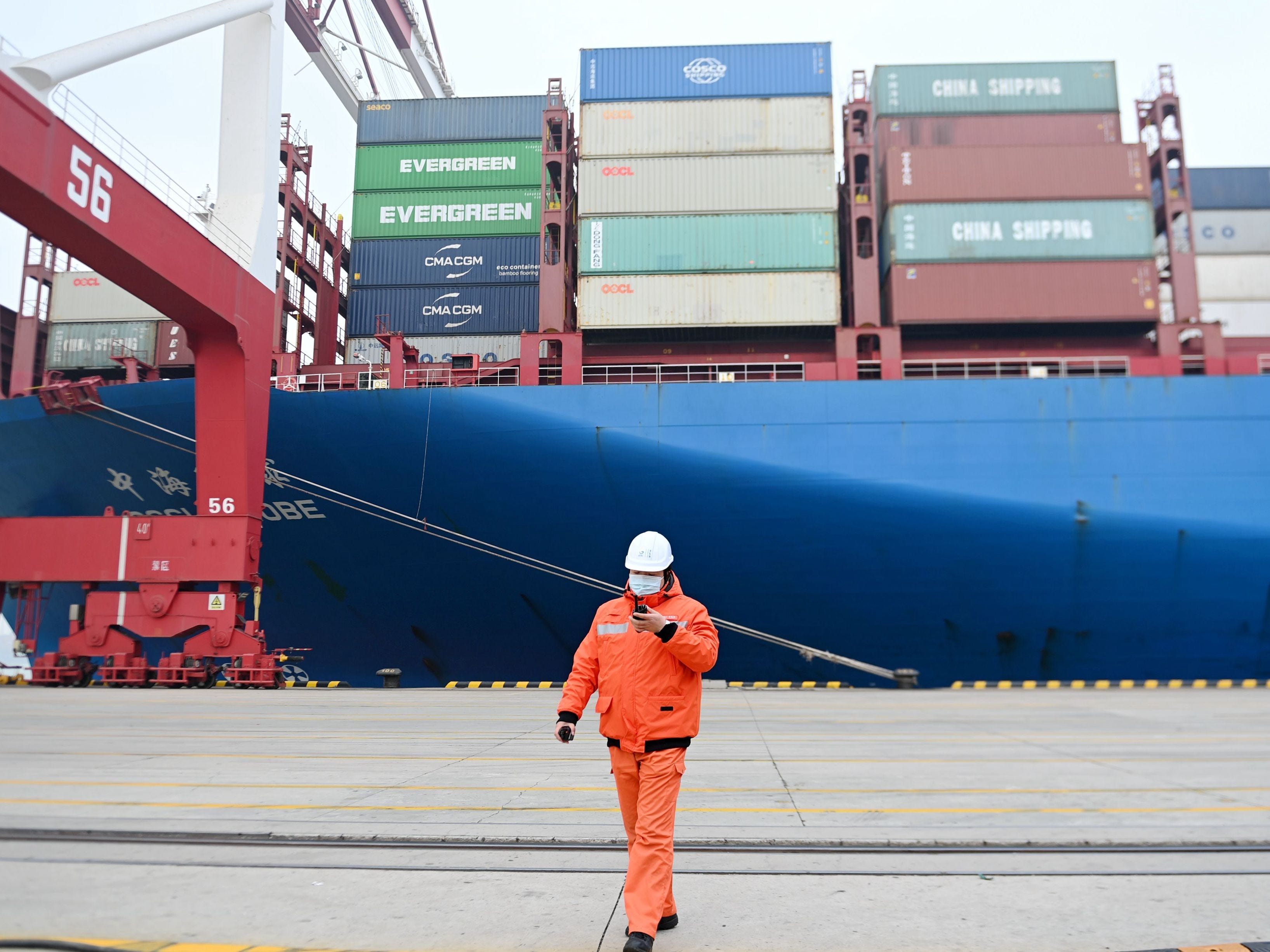 Ein maskierter Mann in Orange vor der Bordwand eines Containerschiffs in China.