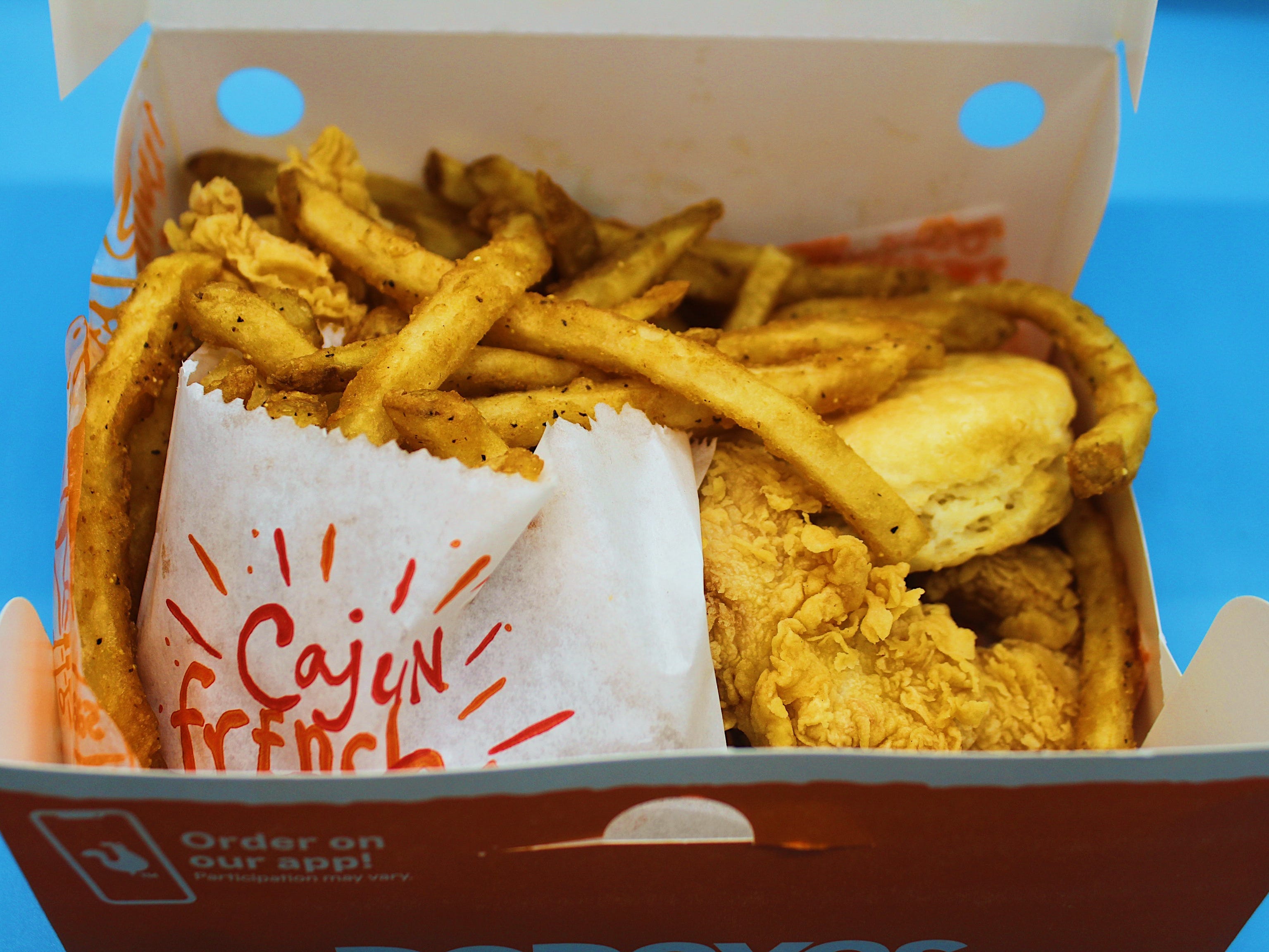 Popeyes-Schachtel mit Cajun-Pommes-Hähnchen-Tender-Keks auf blauem Hintergrund