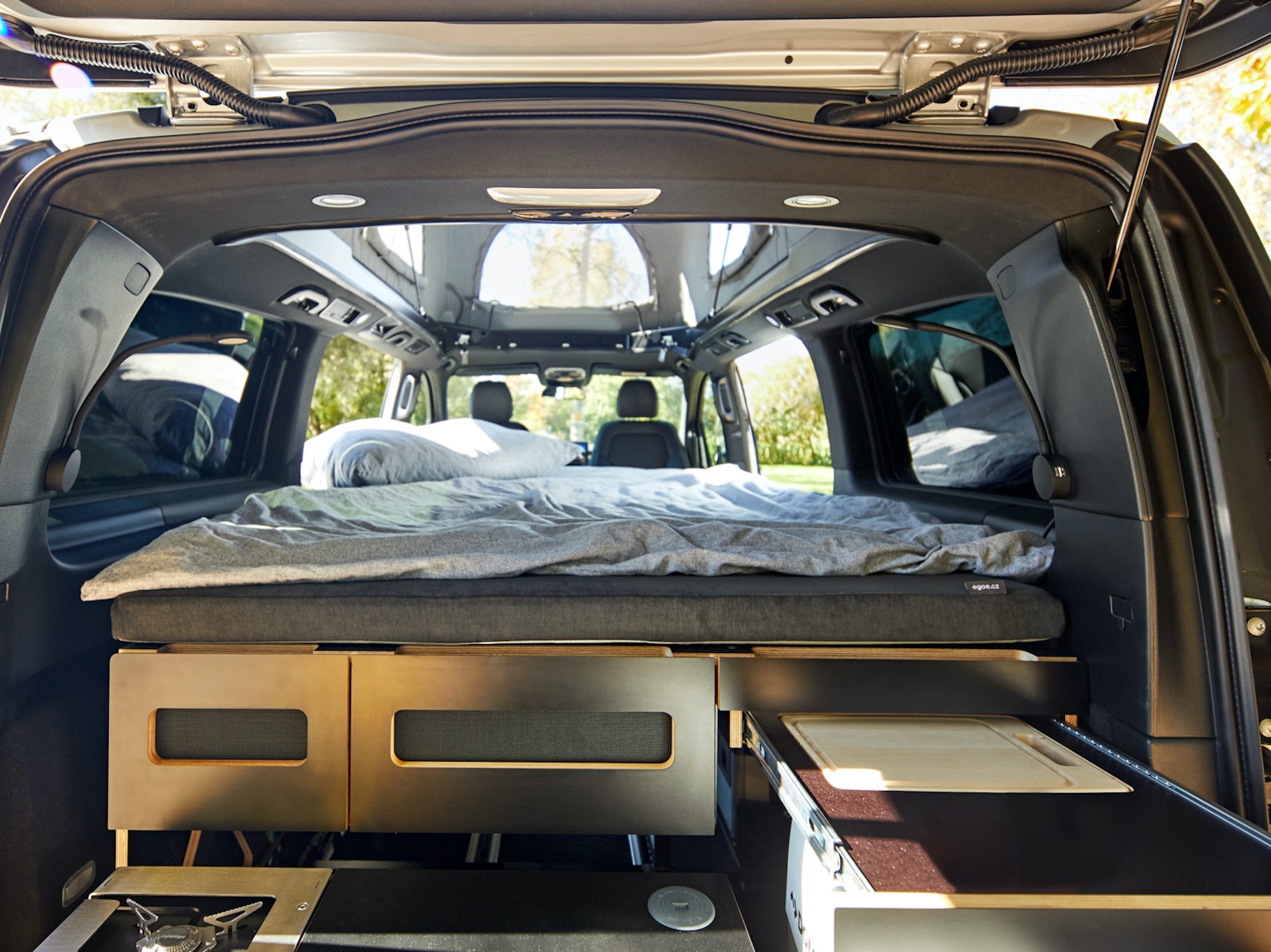Das Innere des Mercedes-Benz EQV mit Schränken und einem Bett darauf in der Nähe des Aufstelldachs des Transporters.