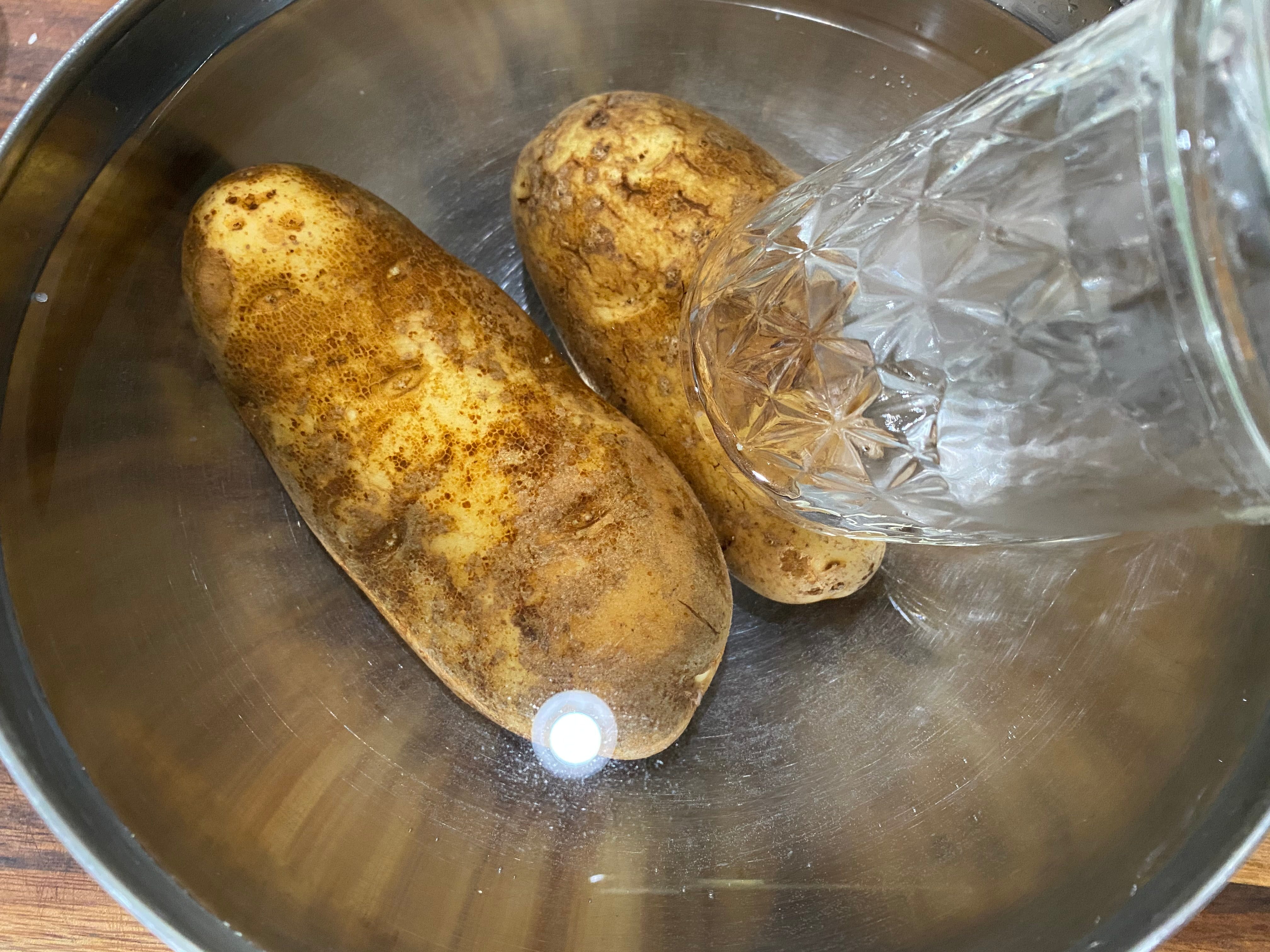 Kartoffeln, die in einer Schüssel mit Wasser sitzen, mit einem Glas, das sie festhält