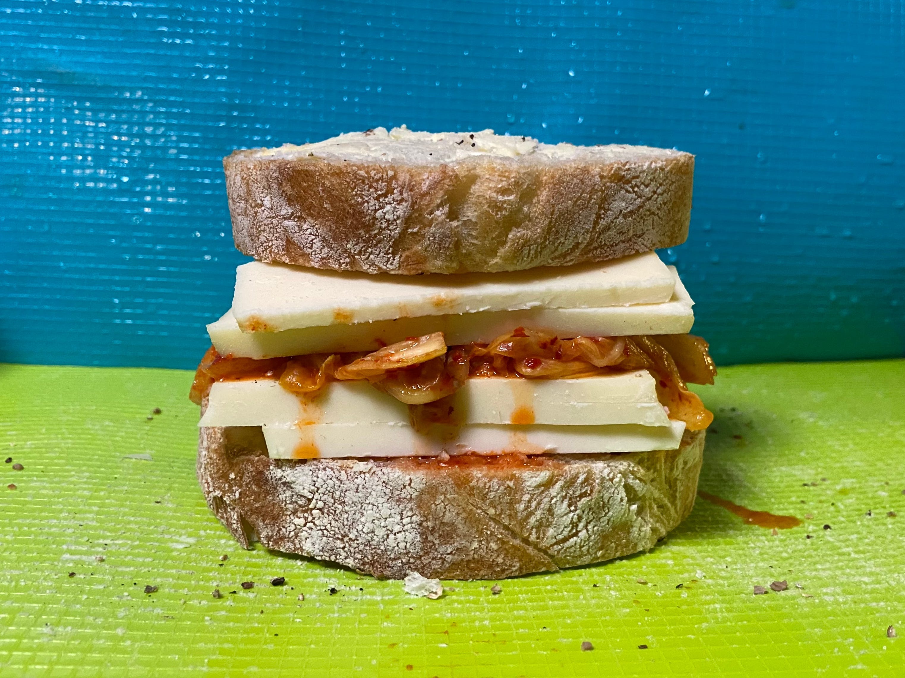 Das zusammengesetzte Sandwich zeigt dickes Brot, Käsestreifen und tropfendes Kimchi.