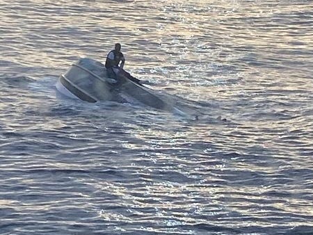 Ein unbekannter Überlebender sitzt auf einem umgestürzten Boot mitten im Ozean