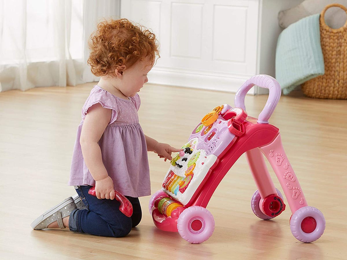 Kleinkind kniet auf Holzboden vor rosa Lauflernspielzeug