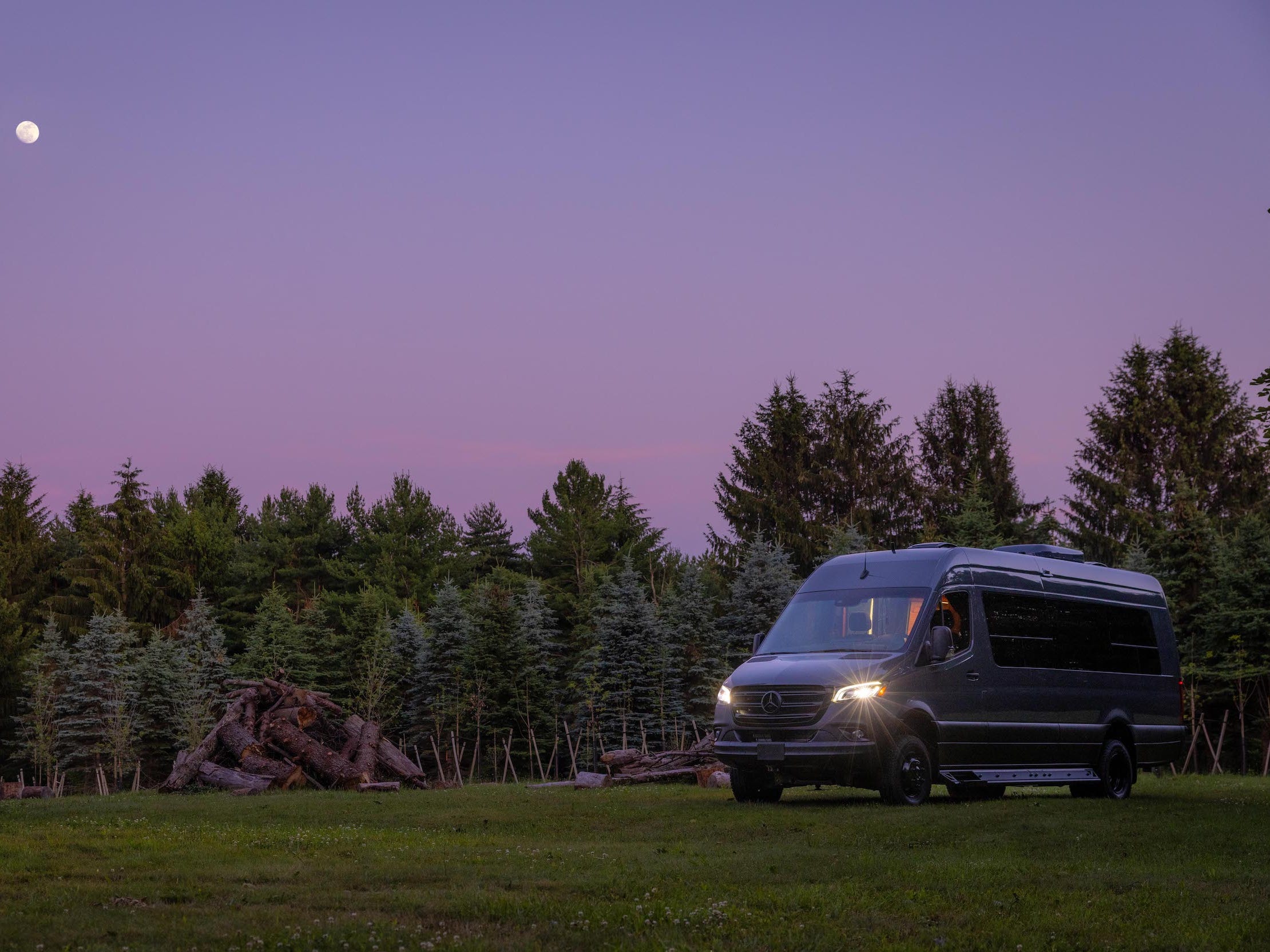 Der Nelson Camper Van draußen in der Abenddämmerung zwischen Bäumen, Natur.