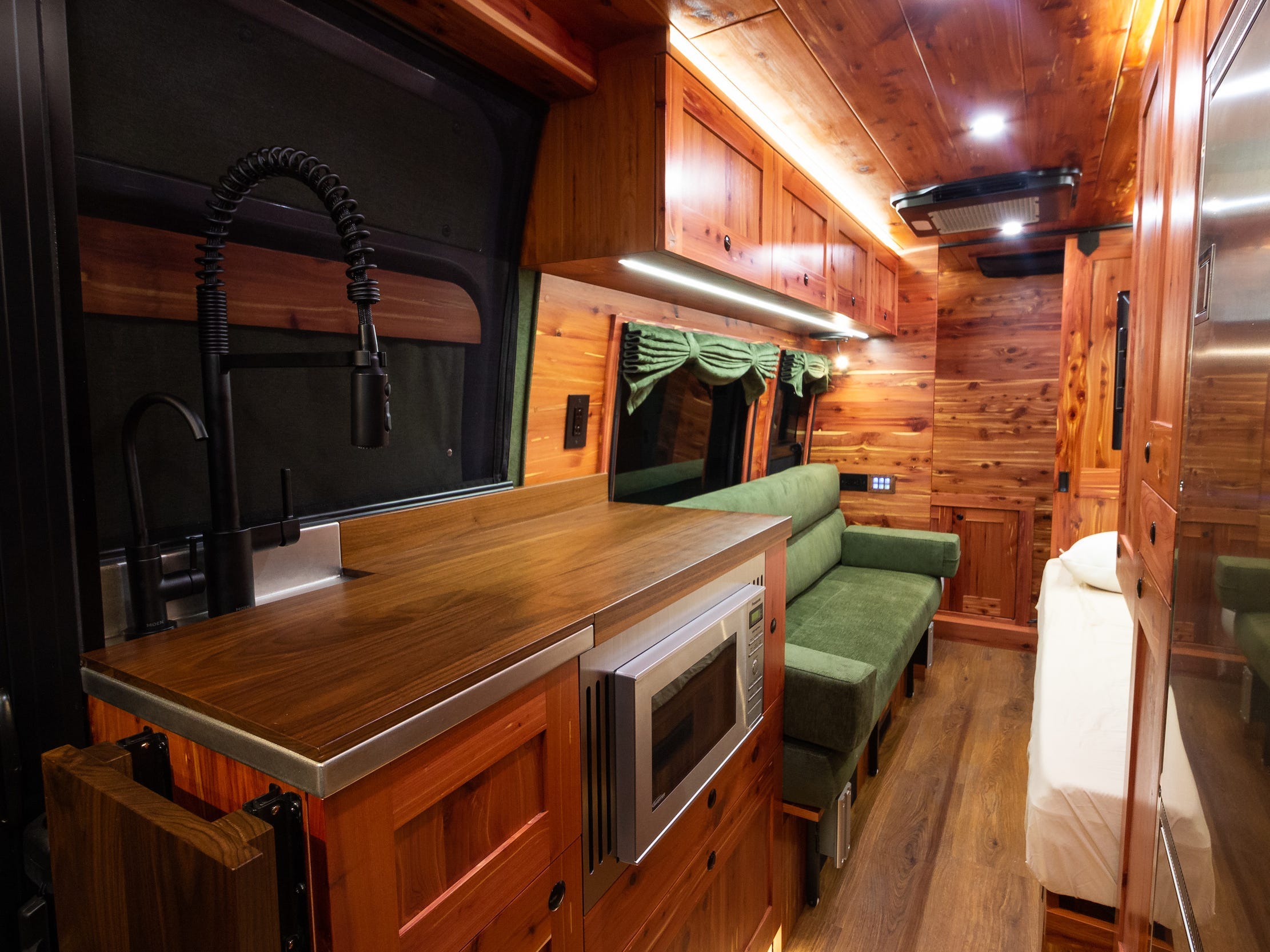 Ein weiter Blick in den Innenraum des Vans zeigt Sitzgelegenheiten, Küche.  Der Innenraum ist mit dunklem Holz ausgekleidet.