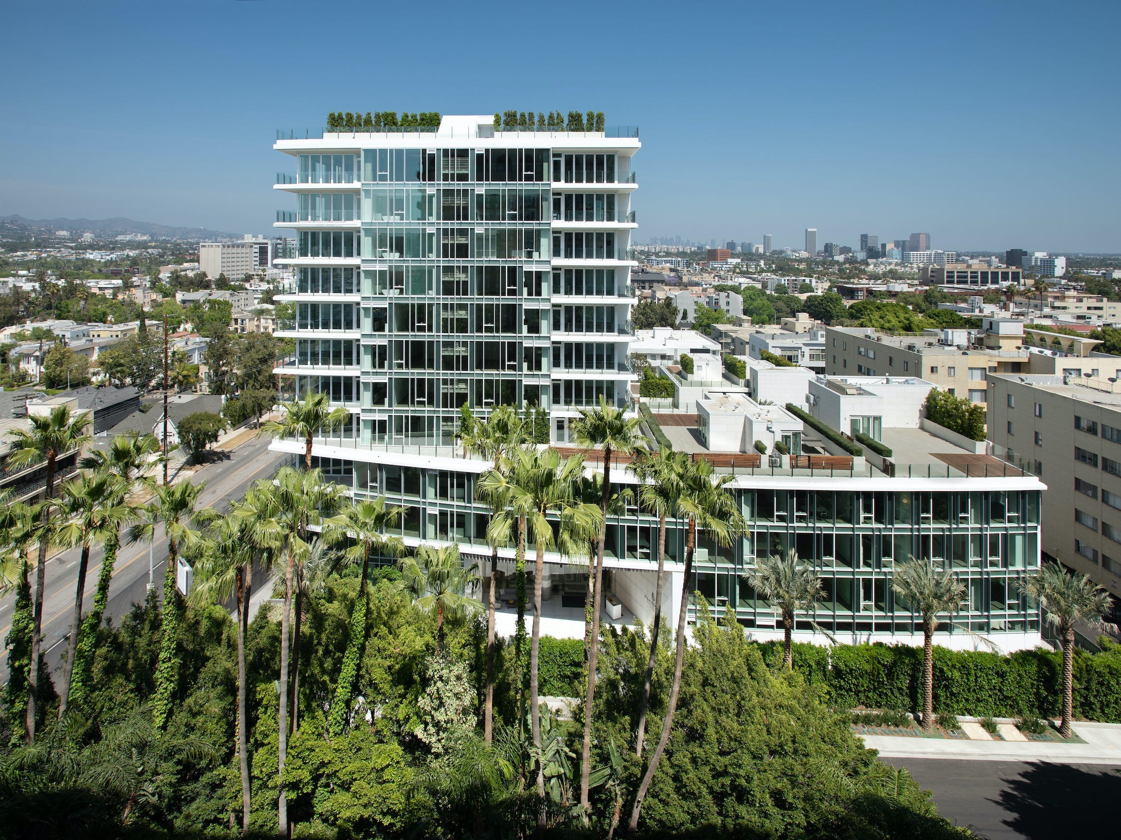 Die Four Seasons Private Residences Los Angeles von Palmen und anderen Gebäuden vor blauem Himmel.