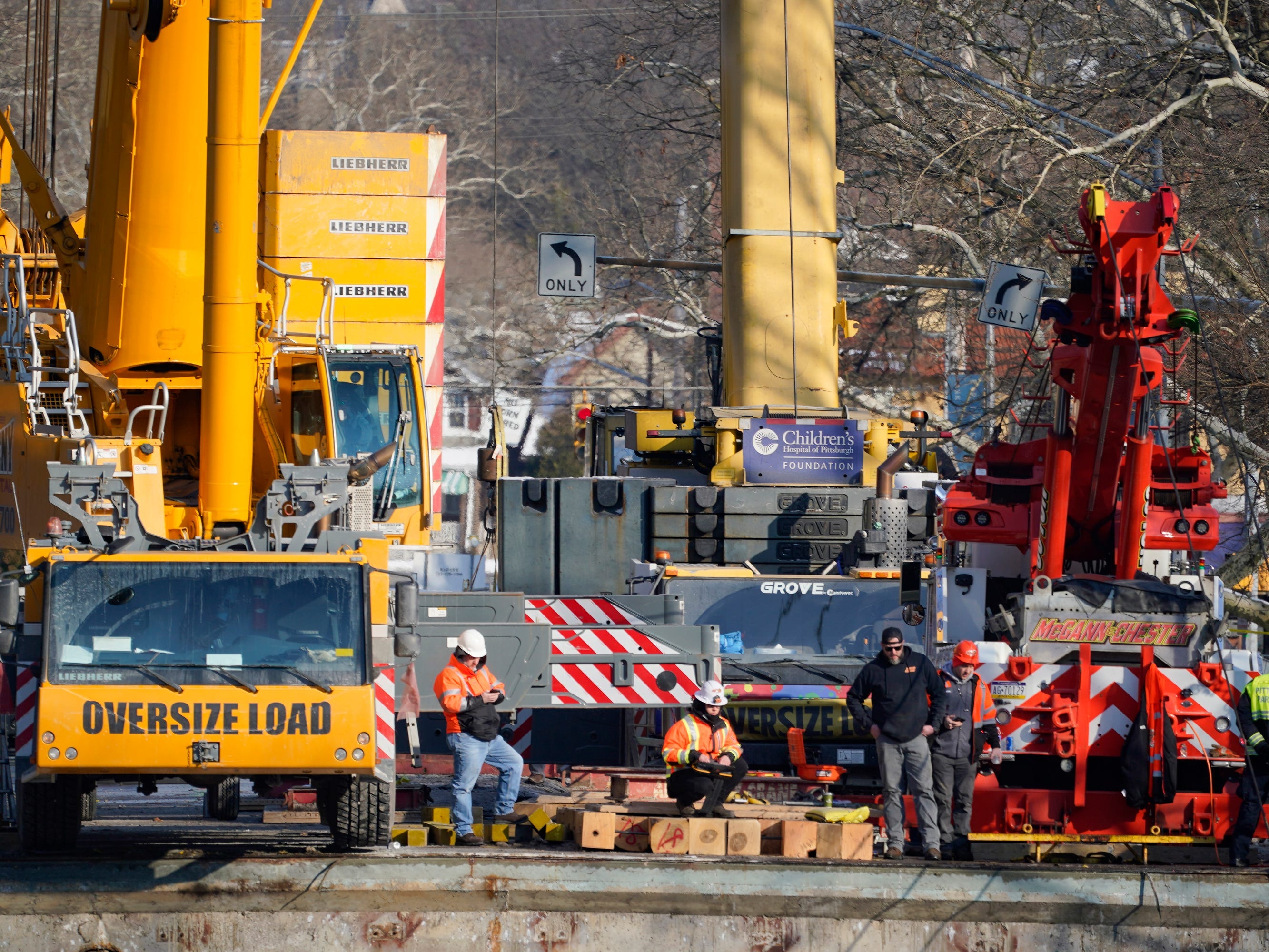 Arbeiter stehen an den Kränen, die verwendet werden, um den Bus zu entfernen, der sich auf einer Brücke befand, als er am Freitag zusammenbrach, während sie daran arbeiten, ihn während des Bergungsprozesses am Montag, den 31. Januar 2022, im East End von Pittsburgh zu entfernen.