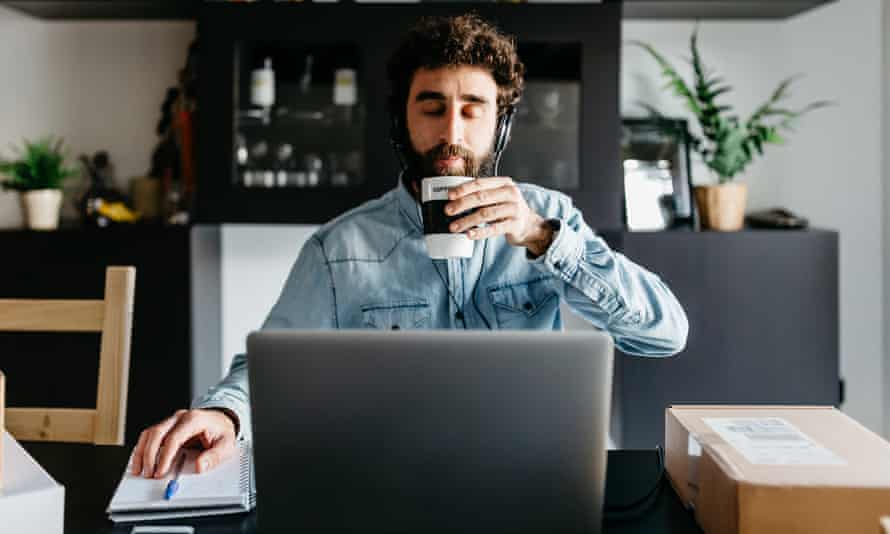 Porträt eines friedlichen Mannes mit geschlossenen Augen in Kopfhörern, der eine Tasse Kaffee am Desktop mit Laptop und Paket im Wohnzimmer trinkt.