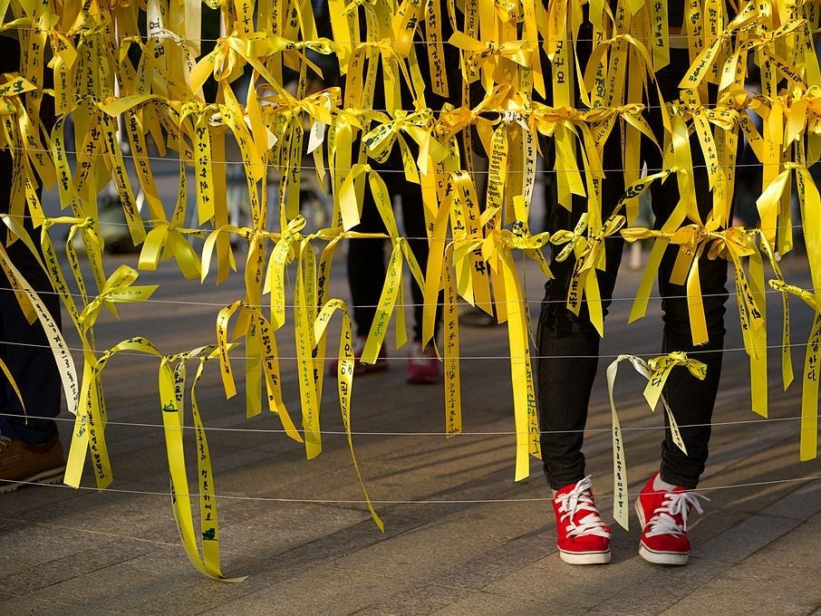 Eine Frau legt am 1. Mai 2014 in Seoul zusammen mit anderen ein gelbes Band an einer Gedenkstätte für die Opfer der Fährkatastrophe „Sewol“ nieder.