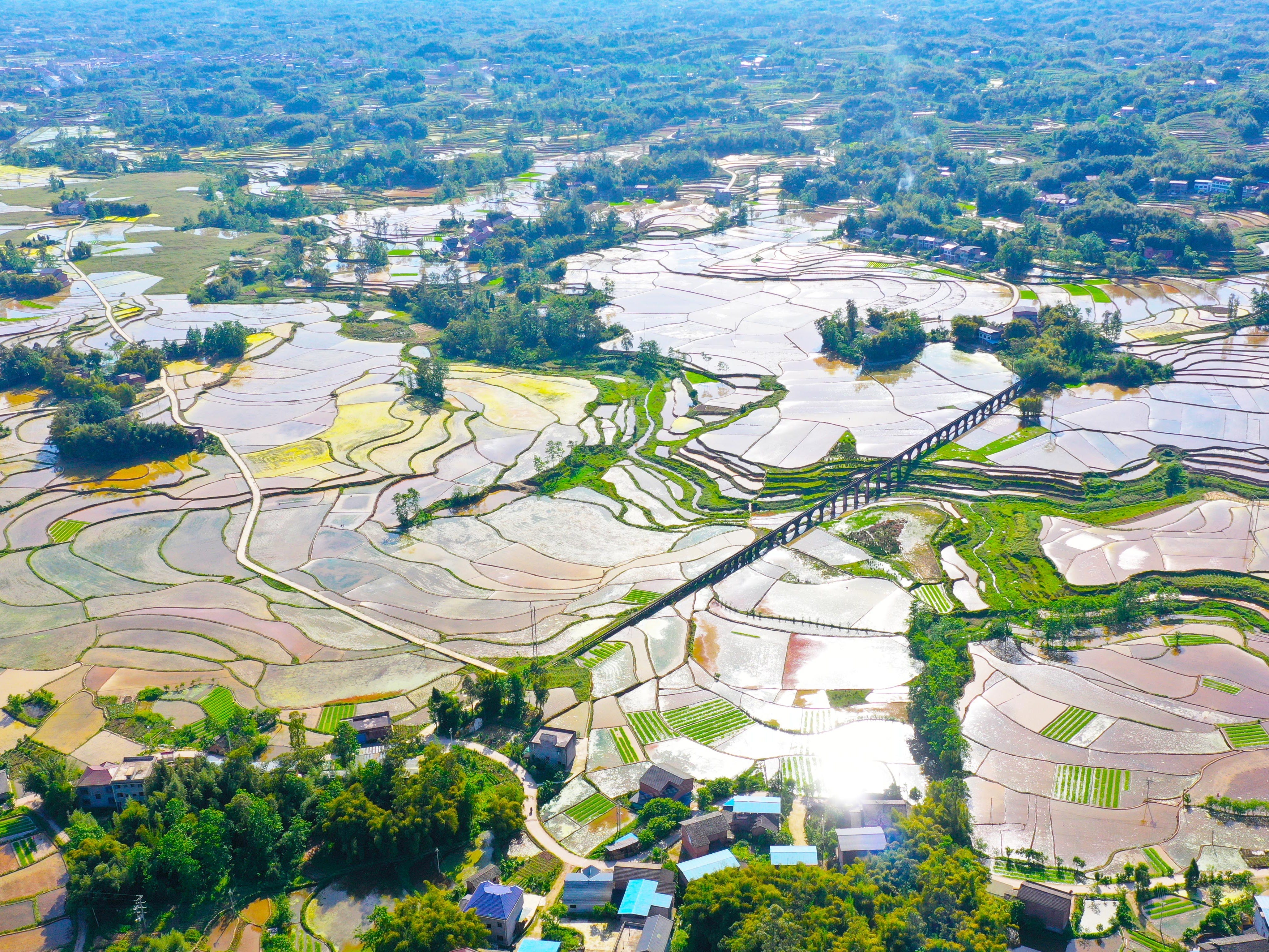 Eine Luftaufnahme zeigt Felder mit entfernten Hügeln, Bäumen, Bauernhäusern und Straßen in Chongqing.