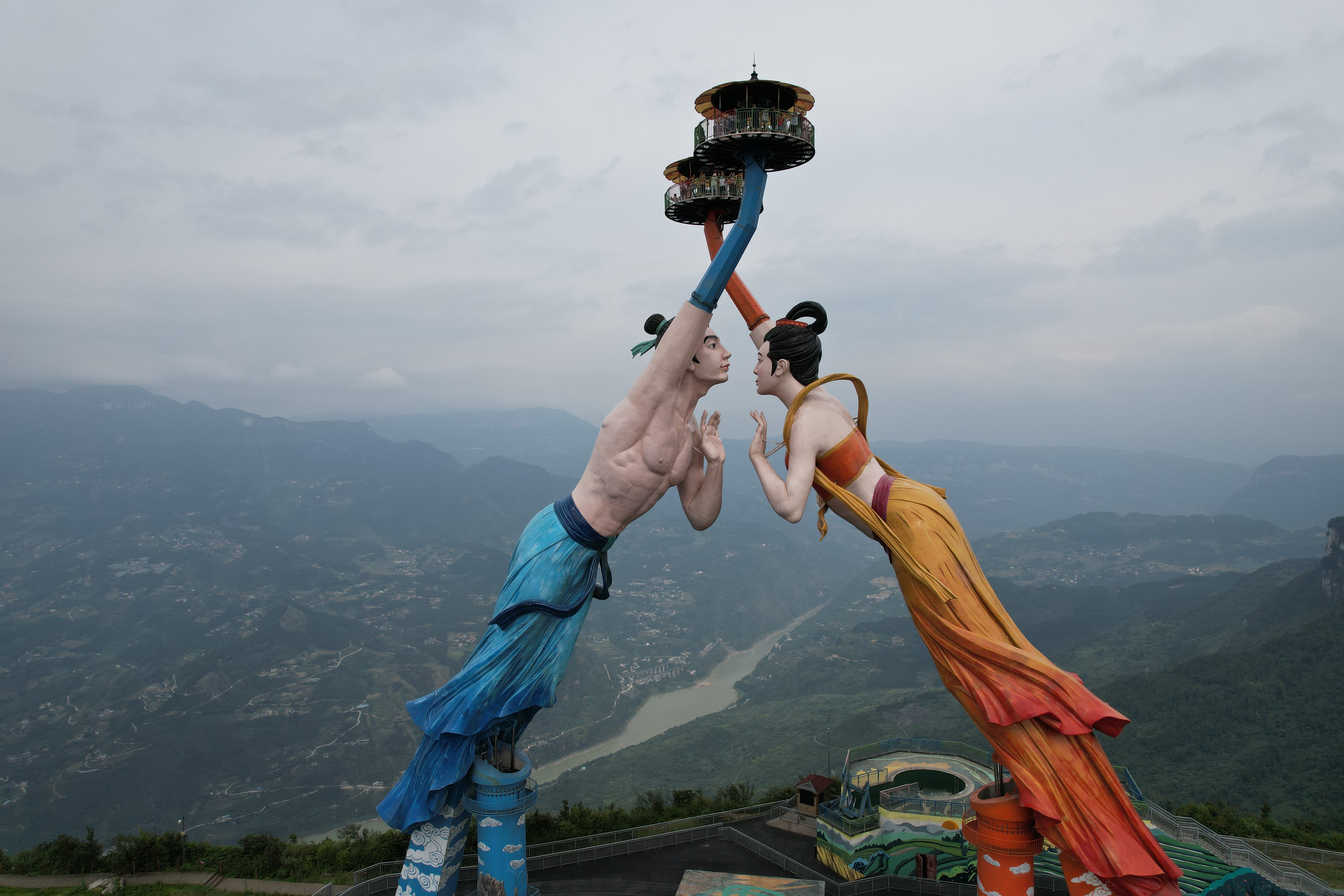 Touristen stehen auf den Aussichtsplattformen in den Händen zweier Roboterskulpturen neben einer Klippe im Baima Mountain Resort