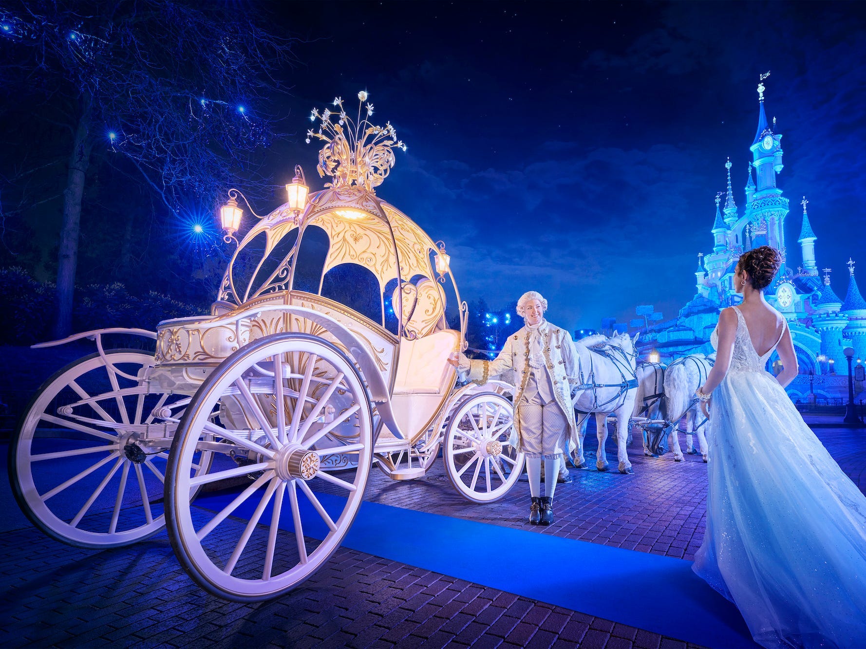 Ein Mann begrüßt eine Frau in einer Kutsche mit einem Schloss im Hintergrund im Disneyland Paris.