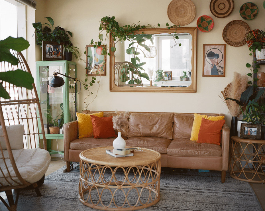 Blick in ein Wohnzimmer mit brauner Ledercouch, Rattanmöbeln und Pflanzen